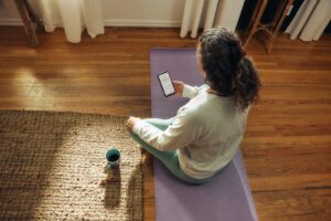 Woman meditating on yoga mat with phone and drink.