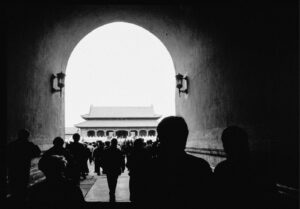 Silhouetted crowd walks through an archway towards a traditional building.