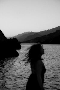 A person in silhouette against a calm lake and distant mountain range