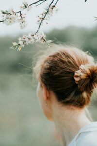 A person with auburn hair in a bun near white cherry blossoms