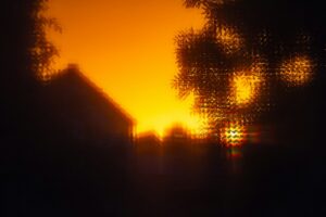 A blurred silhouette of a house and tree against a bright orange sky