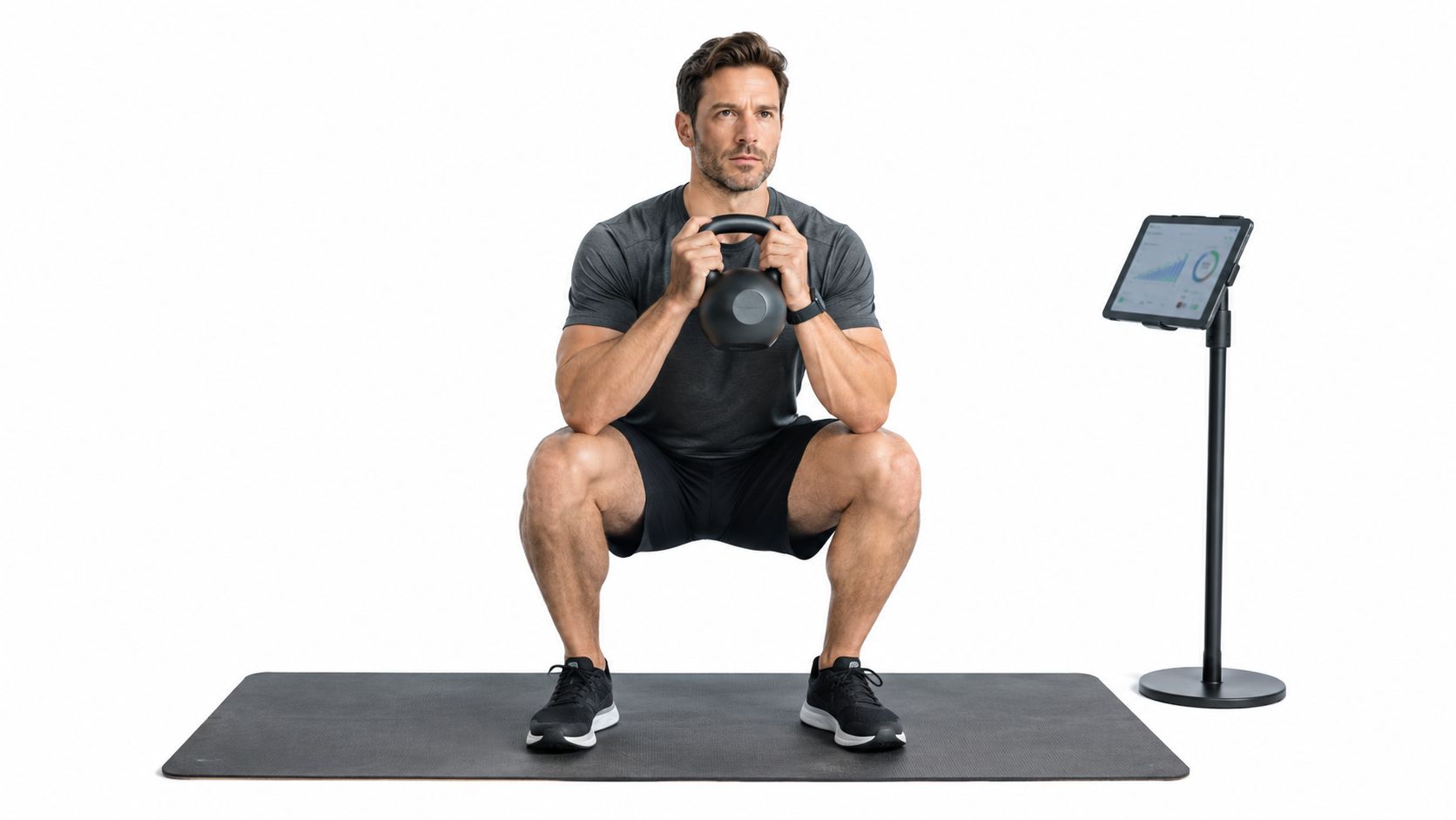 A man performing a kettlebell squat exercise on a fitness mat while viewing data on a tablet
